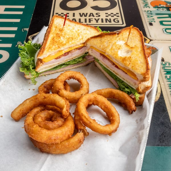 A turkey club sandwich with cheese, bacon, and lettuce, served with golden onion rings.