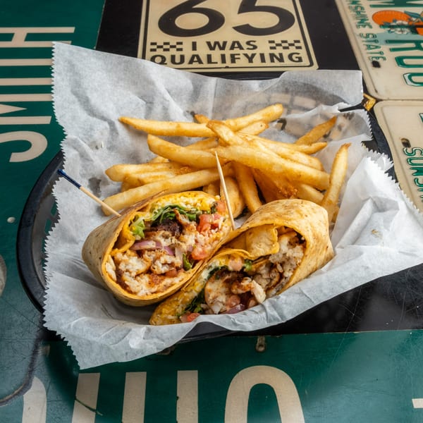 Two halves of a seafood wrap with fries in a basket on a table with license plates.