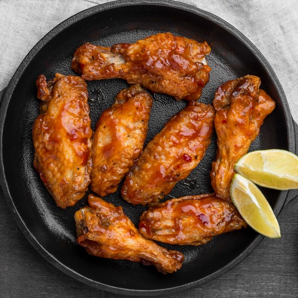 Sweet and spicy chicken wings with lime wedges in a black cast iron pan.