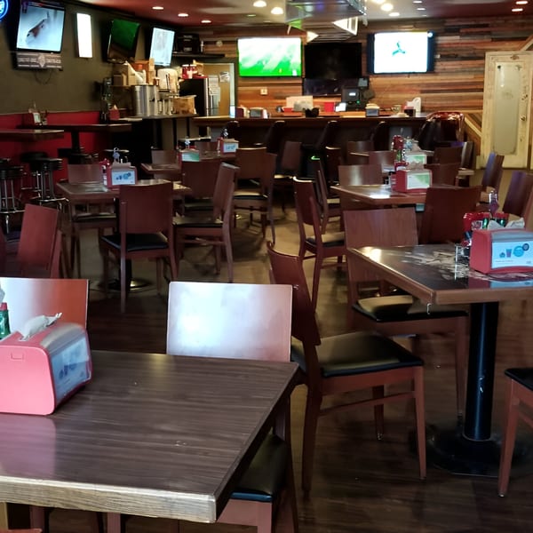 Interior of Nice N Easy Oyster Bar & Grille with empty tables, chairs, a bar, and multiple TVs.