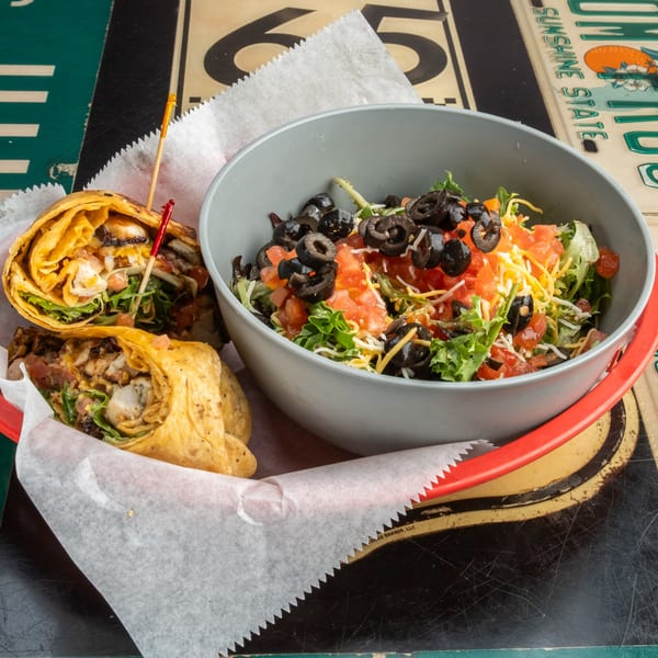 Two grilled chicken wraps and a side salad with olives, tomatoes, and cheese.