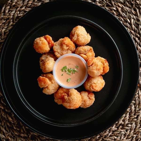Crispy fried shrimp with a side of creamy dipping sauce, garnished with chives, on a black plate.